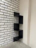 Black wall-mounted shelf against a white brick wall.