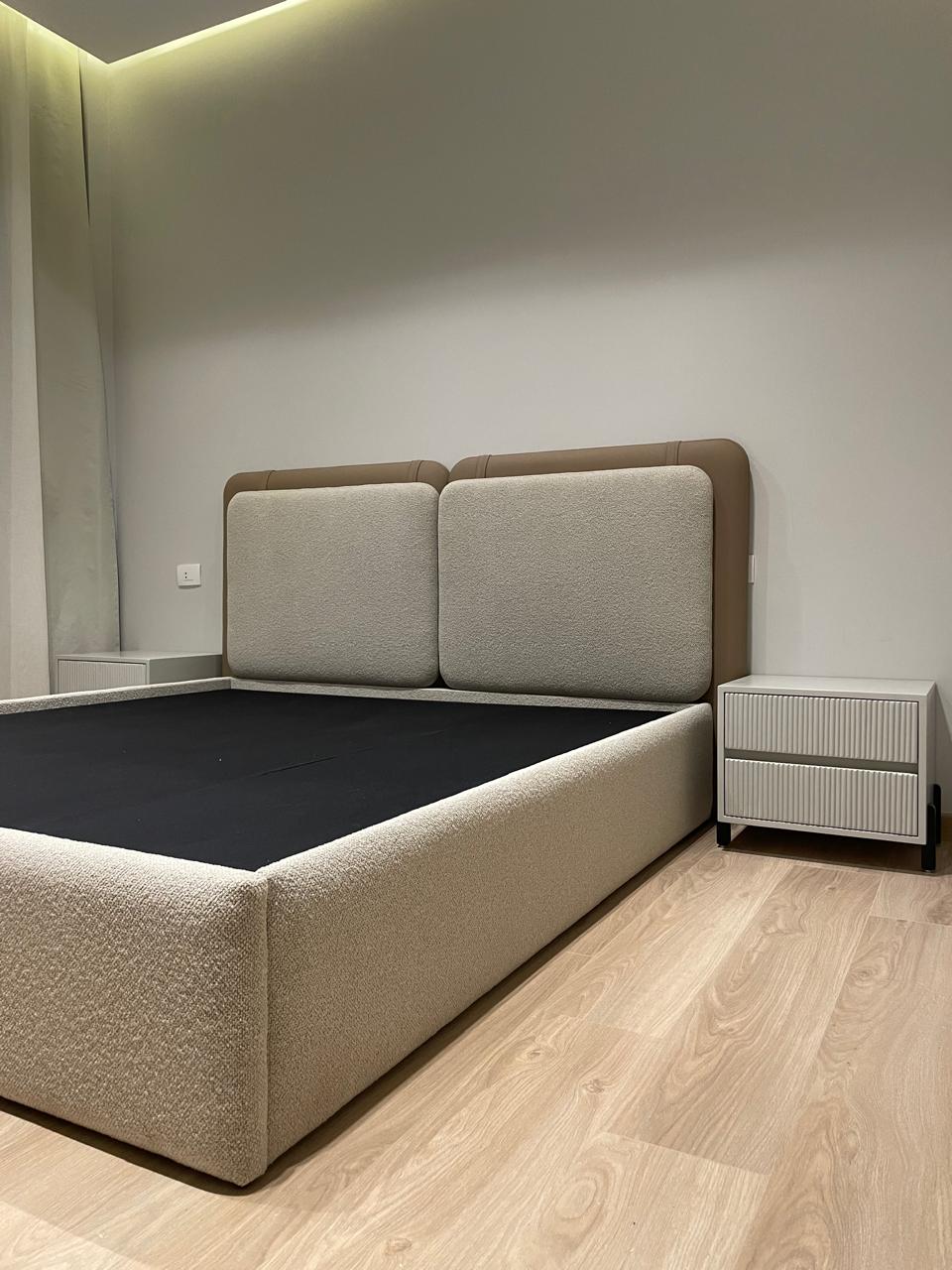 Beige upholstered bed with a matching nightstand in a minimalistic bedroom.