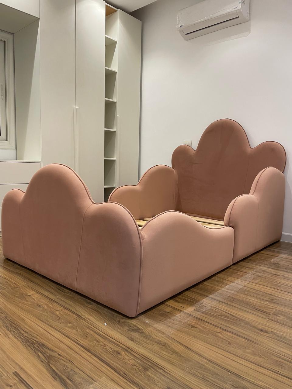 Pink cloud-shaped sofa in a room with wooden flooring and white walls.