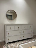 Gray dresser with round mirror on a white wall