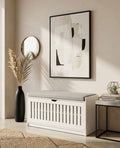 White storage bench in a room with abstract art, vase, and books.