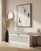 White storage bench in a room with abstract art, vase, and books.